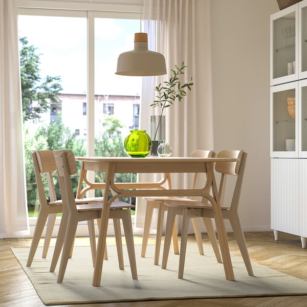 Modern dining table & chairs, green plant, window view, cabinet.