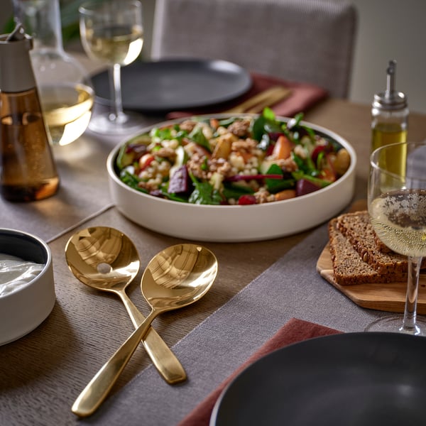 Golden TILLAGD spoons on table with salad bowl and wine glasses.