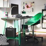 Bright green desk with monitor, lamp, keyboard, mouse, and speaker. Black and white patterned bag, with bookshelf and colorful wall organizer behind.