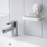 A modern bathroom sink with a chrome faucet and a white soap dish attached to the wall using a suction cup. A bar of soap rests in the dish.