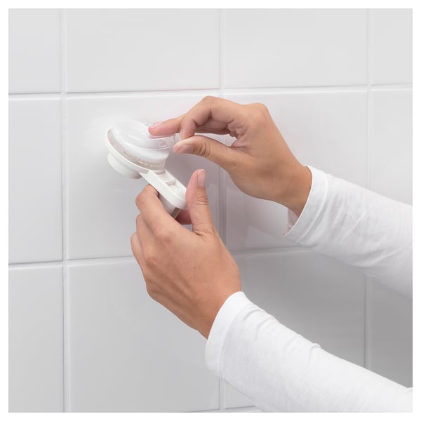 Person installs white TISKEN toilet paper holder with suction cup on tiled wall.
