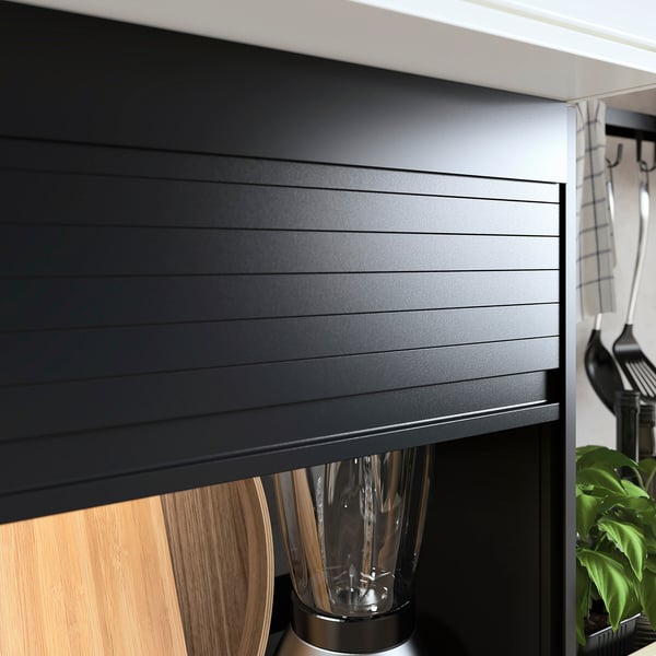 Black kitchen cabinet with sleek, horizontal lines and a smooth tambour door. Stainless steel appliances stored inside.