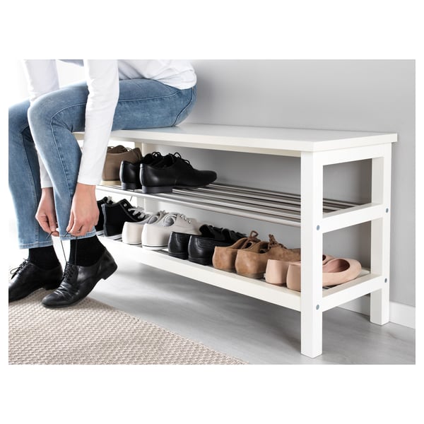Person sitting on a white TJUSIG shoe bench, organizing black shoes on the shelf.