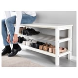 Person sitting on a white TJUSIG shoe bench, organizing black shoes on the shelf.