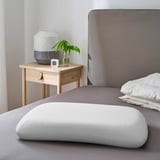 Modern bedroom with ergonomic pillow, nightstand with lamp and plant.