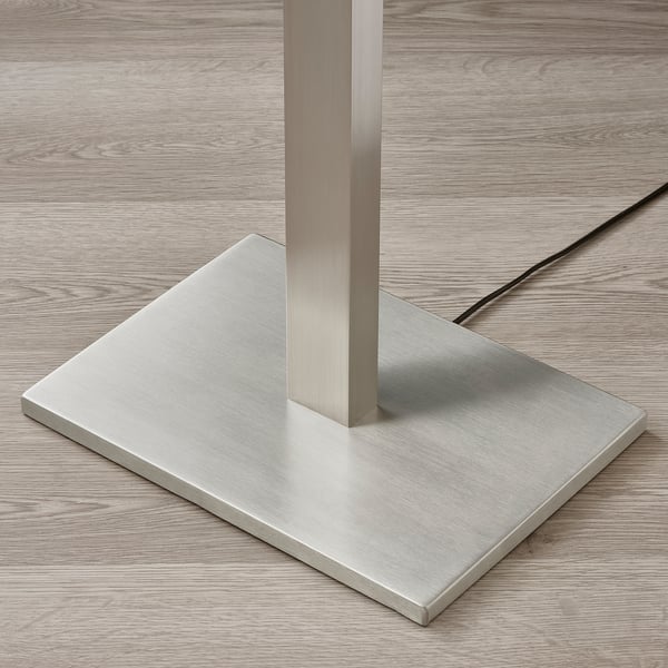 Modern metal floor lamp with thick, sturdy base, standing on wooden surface.