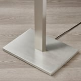 Modern metal floor lamp with thick, sturdy base, standing on wooden surface.