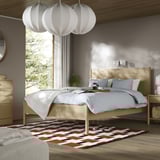 Bedroom with TONSTAD bed, wood finish, colorful rug, blue sheets, white pendant lamps.