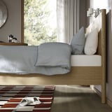 Clean, minimalist bedroom with wooden bed, blue comforter, and slippers on striped rug.