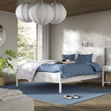 A modern off-white TONSTAD bed frame with a blue rug, stylish lamps, and plants. Clean and minimalist, its spacious compared to other items.