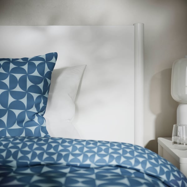 Bed with off-white frame, blue patterned duvet, white pillow. Sturdy, adjustable sides for various mattress thicknesses.
