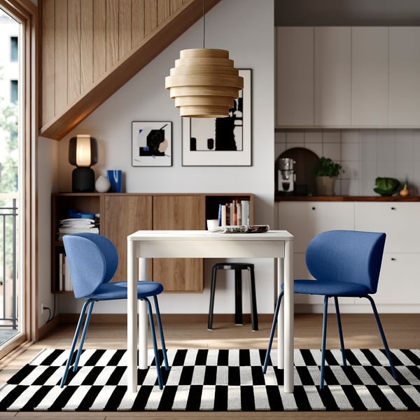 Modern dining area with white TONSTAD extendable table, blue chairs, black-white striped rug, wooden paneling, and unique light fixture.