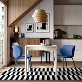 Modern dining area with white TONSTAD extendable table, blue chairs, black-white striped rug, wooden paneling, and unique light fixture.