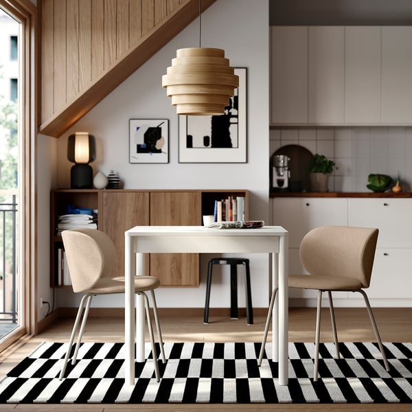 Modern dining area with TONSTAD white table and beige chairs on black and white rug, wooden accents, understairs storage, and hanging lamp.