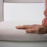 Hand resting on soft, textured white cushion. Chunky knit blanket nearby, illustrating comfort and quality.