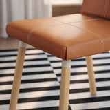 Close-up of TONSTAD chair: orange-brown upholstery, wooden legs, striped floor.