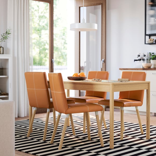 Oak dining set with burnt orange chairs, surrounded by windows, decorated with oranges, striped rug, and pendant light.