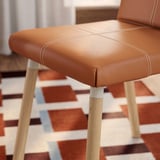 Close-up of a stylish, cushioned chair with smooth, light wood legs and detailed stitching.