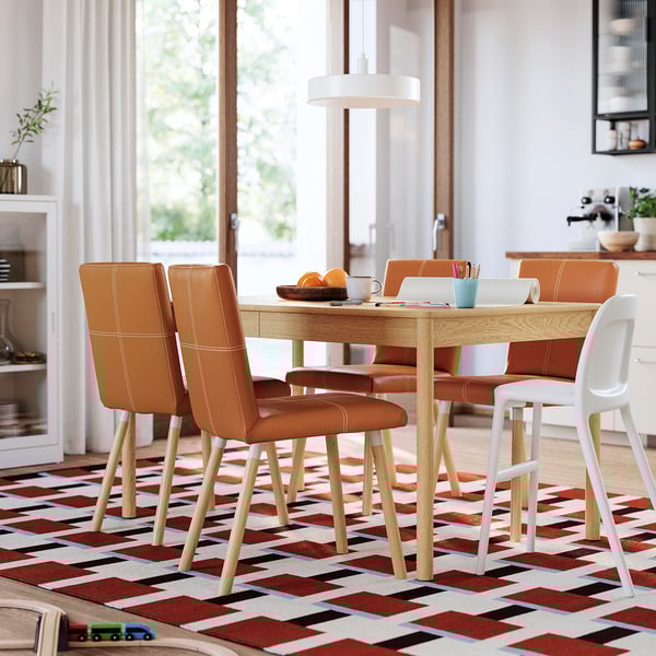 Modern dining set with orange leather chairs, wooden table, and multi-colored rug.