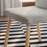 Modern chair with gray tweed seat, wooden legs, on striped floor.