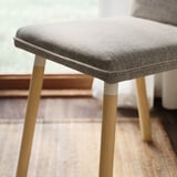 Modern stool with gray fabric seat, light wooden legs.