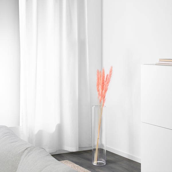 Minimalist room, white couch, dried orange stems in glass vase by window.