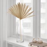 Glass vase with dried palm leaf on windowsill.