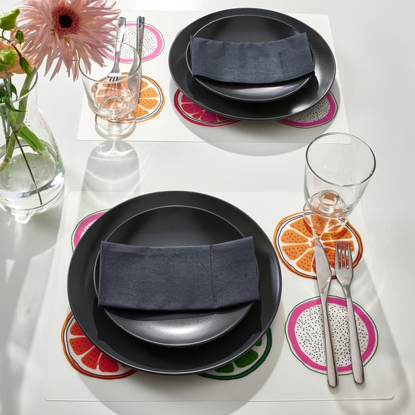Brightly colored place mats with citrus slices create cheerful table settings. Black plates, cutlery, and glasses complete the modern look.