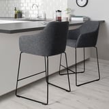 Two TOSSBERG barstools with grey fabric and black metal legs under kitchen counter, ergonomic backs.
