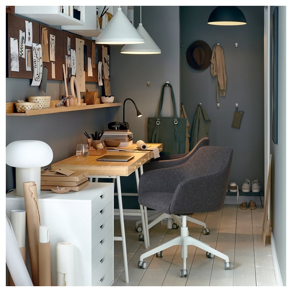 Home office with TOSSBERG chair, desk, lamp, and wall hooks. Grey chair, wooden desk, grey walls, and white pendant light.
