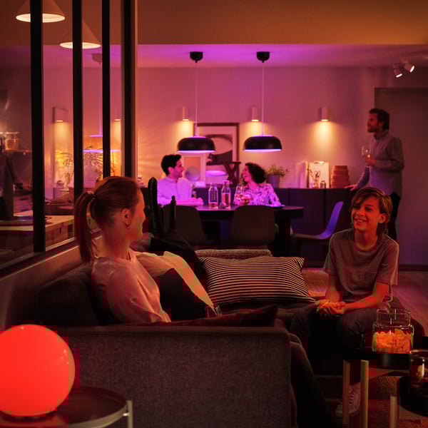 Modern bar with patrons enjoying drinks under warm, orange-hued lighting while two sit on a couch.