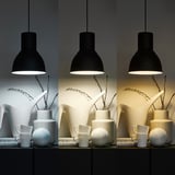 Three pendant lamps with warm-to-cool light. Below, white ceramic vases, mugs, and sphere, light shifts left to right.