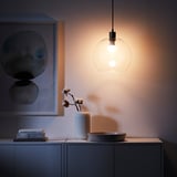 Modern kitchen corner with hanging TRÅDFRI light, soft glowing bulb, grey storage, white vase with cotton flower, and abstract art.