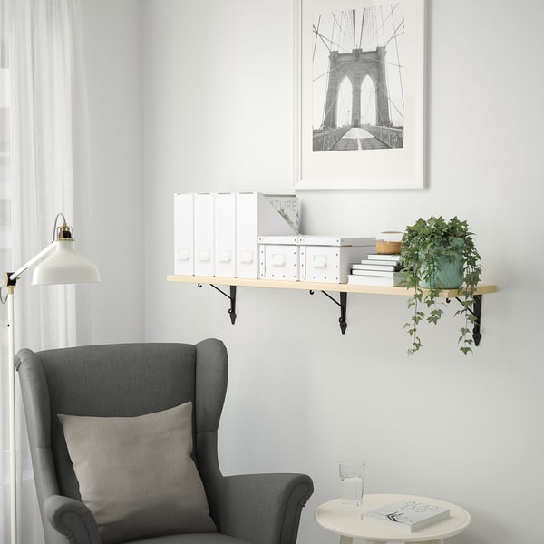 Minimalist reading nook: gray chair, floating shelf with white decor, hanging plant, brooklyn bridge art.