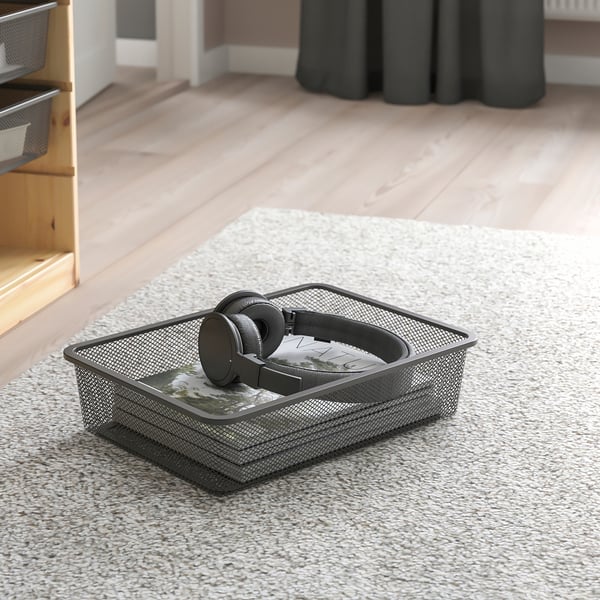 Mesh storage box on carpet, containing headphones and box. Part of TROFAST series for organizing items.