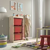 Kids room with TROFAST storage & red boxes. Near art, coats, and books table. Tall storage.
