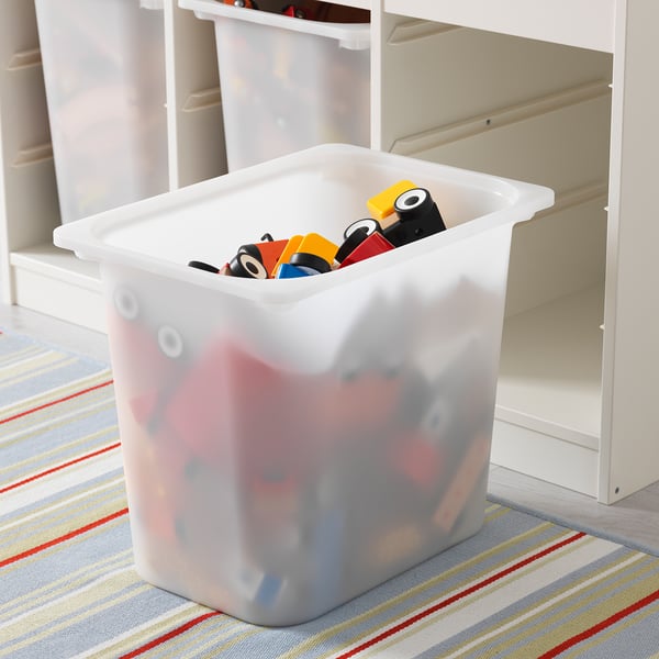 Plastic storage box filled with colorful building blocks on striped rug near white storage unit.