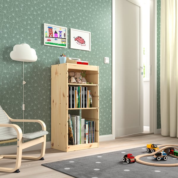 Childs room with TROFAST light wood storage shelf holding books and toys. Bright wallpaper, rug, and floor lamp. Toy cars and chair visible.