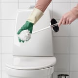 Person cleaning a toilet with a white brush wearing green gloves.