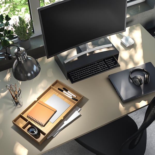 Modern office desk, black, with computer setup. Includes keyboard, monitor, mouse, headphones, notebook, pens, lamp, and plant.