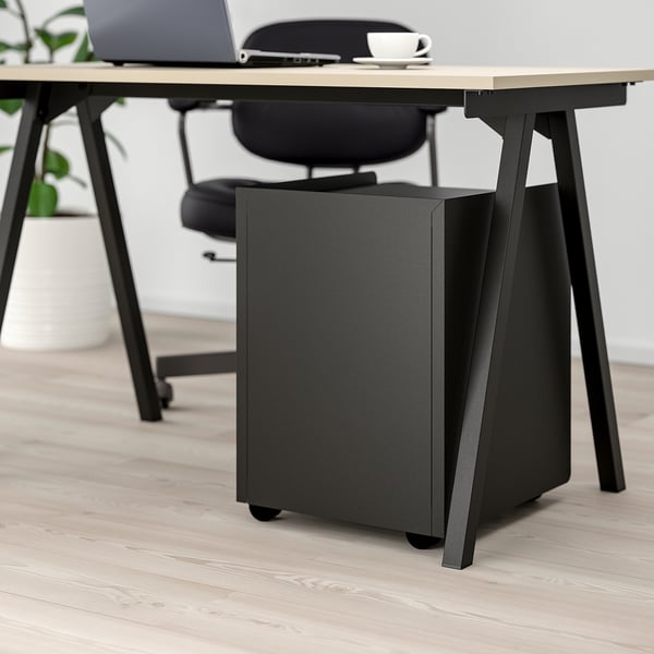 Black office chair, desk with laptop, cup, notebook, and storage unit.