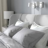 Cozy bed with curved headboard, soft pillows, and nightstand with lamp.