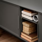 Black metal tv stand with handle; open shelf holds books and woven basket, closed sections hide storage.