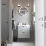 Minimalist bathroom: round mirror, concrete vanity, glass shower, wall towels, plant.