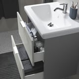 Modern bathroom with TVÄLLEN sink, open drawer showing toiletries, fits base cabinet, includes drain stopper.