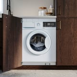 A white built-in washing machine nestled between wooden cabinets with a control panel and laundry detergent on top.