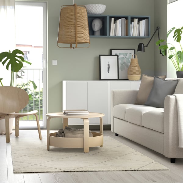 Modern living room with grey rug, wooden coffee table, sofa, wicker lamp, and plants.