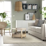 Modern living room with grey rug, wooden coffee table, sofa, wicker lamp, and plants.