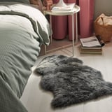Bedroom scene with white bed, gray blanket, round white side table, pink curtains, books, and a thick gray rug on the floor.