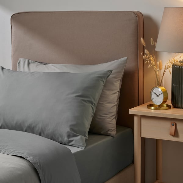 Ullvida grey pillowcase in cotton/lyocell blend by bed, rectangular shape, soft & durable. Larger than clock and lamp on wooden nightstand.